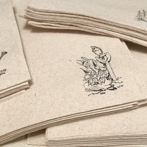 May include: A stack of beige paper cards with black ink illustrations of rabbits and gardening tools. The illustrations include a watering can, a rabbit with a shovel, and a rabbit near a fence. The cards have a rustic, handmade appearance.