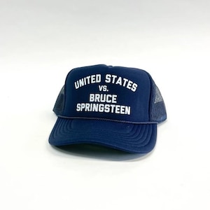 Puede incluir: Una gorra de camionero azul marino con un logotipo bordado en blanco que dice "United States vs. Bruce Springsteen".