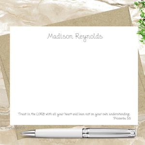 May include: A white card with a brown border and the text "Madison Reynolds" at the top. The card has a quote from Proverbs 3:5, "Trust in the LORD with all your heart and lean not on your own understanding." A white pen is lying on the card.