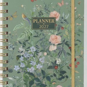 May include: A sage green spiral-bound planner for 2027 featuring a botanical print with pink roses, blue wildflowers, various green leaves, small red berries, and several butterflies and birds scattered across the front cover.