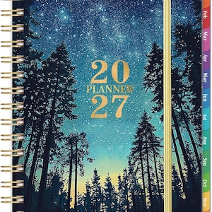 May include: A spiral-bound 2027 planner featuring a dark blue night sky filled with stars above a silhouette of pine trees. The cover displays the text 20 PLANNER 27 in gold lettering, with a gold elastic band and colorful monthly tabs.