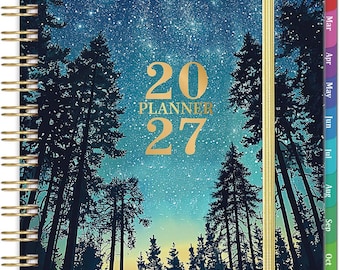 May include: A spiral-bound 2027 planner featuring a dark blue night sky filled with stars above a silhouette of pine trees. The cover displays the text 20 PLANNER 27 in gold lettering, with a gold elastic band and colorful monthly tabs.