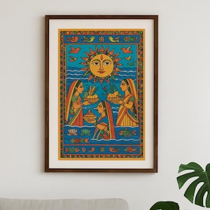 May include: A framed art print with a colourful illustration of a religious scene. The artwork shows three women in traditional dress offering baskets of fruit and flowers to a large sun. The background is bright blue with decorative elements.