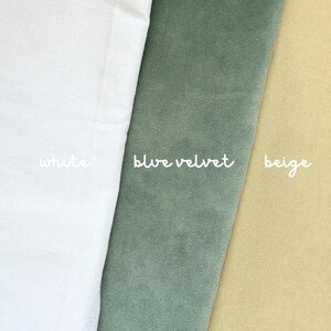 May include: An image showcasing three fabric swatches. The swatches are white, blue velvet, and beige. The names of the colors are written in cursive script on each swatch. The fabrics are folded and layered.