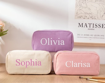 May include: Three personalized makeup bags in different colors. The bags are made of corduroy fabric and have the names Olivia, Sophia, and Clarisa embroidered on them in white.