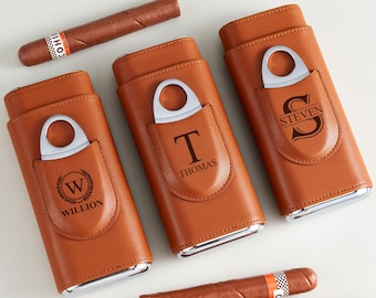 May include: Three brown leather cigar cases with silver accents and built-in cigar cutters. Each case is personalized with a different name or initial: "W WILLION", "T THOMAS", and "STEVEN". Two cigars are also visible.