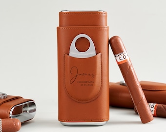 May include: A brown leather cigar case with a silver cigar cutter in the front pocket. The case is personalized with the name "James" and the text "Groomsman 12-23-2025". A cigar rests against the case. Other cigar cases are in the background.