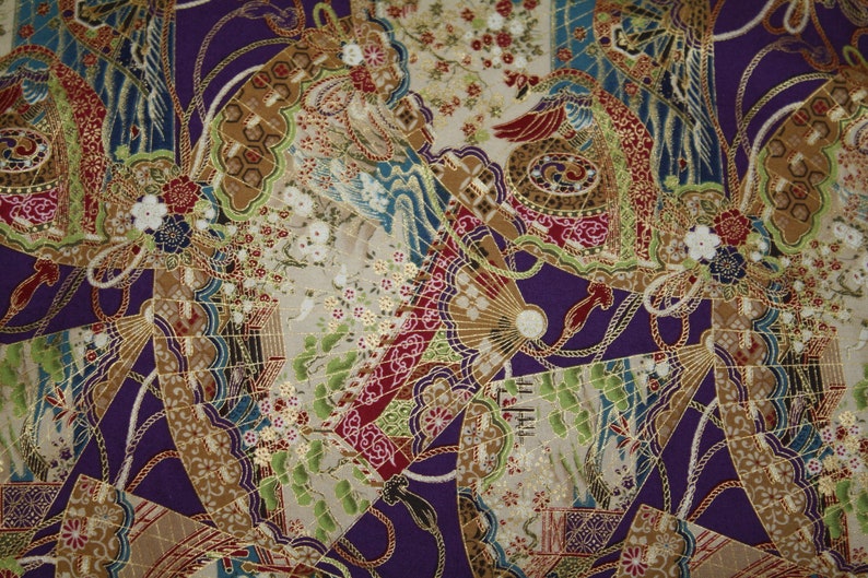May include: A patterned fabric with a repeating design of fans, flowers, and birds in purple, gold, red, green, and blue. The fabric has a textured appearance with intricate details.