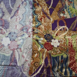 May include: Close-up of a patchwork textile with floral and geometric patterns. The fabric displays a mix of colours, including purple, gold, green, and white. The design incorporates elements of traditional Japanese art.