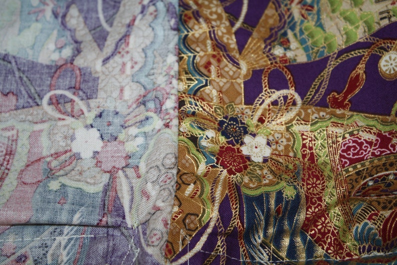 May include: Close-up of a patchwork textile with floral and geometric patterns. The fabric displays a mix of colours, including purple, gold, green, and white. The design incorporates elements of traditional Japanese art.