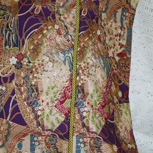 May include: Close-up of a patterned fabric with a vibrant design. The fabric features a mix of colours, including purple, beige, and green, with a repeating pattern of fans, flowers, and other decorative elements. A green cord runs vertically down the centre.