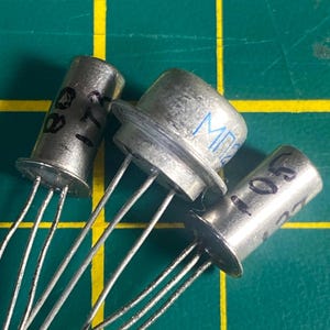 May include: Three silver transistors with black markings. The transistors are on a green grid surface. The text on the transistors reads "2N711" and "MP350".