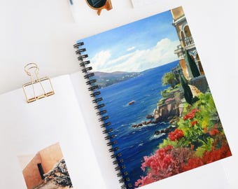 Könnte beinhalten: Spiralgebundenes Notizbuch mit einem lebendigen Gemälde einer Küstenlandschaft. Das Kunstwerk zeigt ein blaues Meer, einen klaren Himmel und ein Gebäude mit roten Blumen. Das Notizbuch liegt offen auf einer weißen Oberfläche, mit einer goldenen Büroklammer und einer Sonnenbrille in der Nähe.