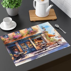 May include: A watercolor illustration of a Parisian cafe with blue and white awnings, flowers in window boxes, and tables and chairs set up outside. The cafe is painted in a light yellow color with a brown door and windows. The scene is set on a sunny day with a blue sky and white clouds.