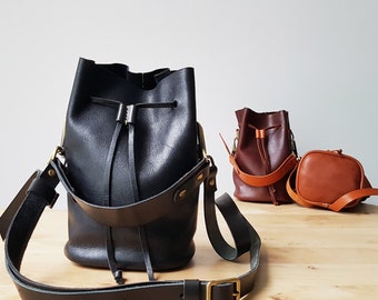 May include: Two black leather bucket bags with adjustable straps. One bag has a brown leather strap and a brown leather bucket bag.