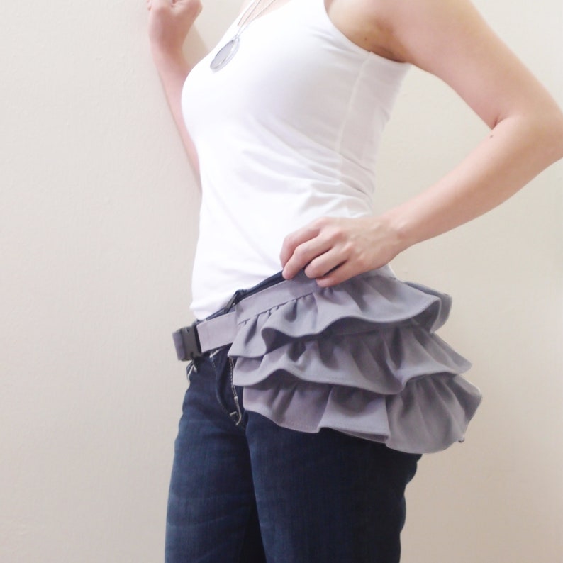 May include: A gray ruffled fabric belt worn over a pair of blue jeans.