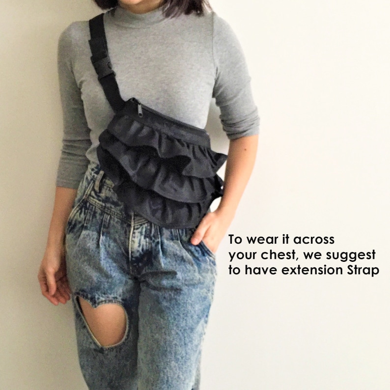 May include: A black ruffle fanny pack worn across the chest. The bag has a zipper closure and is worn with a gray long-sleeve shirt and blue jeans.