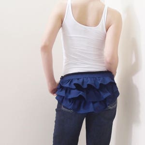 May include: A navy blue ruffled skirt with a black waistband. The skirt is worn over a pair of blue jeans.