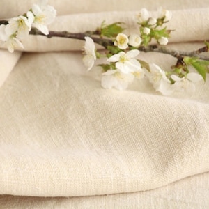 May include: A close-up of a white linen fabric with a branch of white blossoms. The fabric is folded and the blossoms are arranged on top of the fabric.