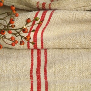 May include: A close-up of a folded linen fabric with red stripes. The fabric is textured and has a natural, rustic look. A sprig of red berries is resting on the fabric.