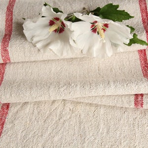May include: White fabric with red stripes, folded in layers. Two white flowers with red centers are placed on top of the fabric.