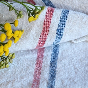 May include: A white linen tea towel with red and blue stripes. A bouquet of yellow flowers is placed on top of the towel.