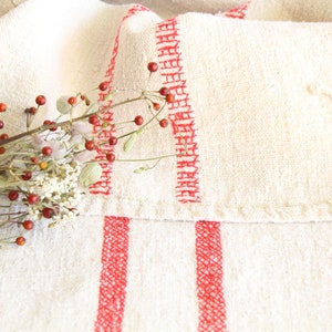 May include: A white linen tablecloth with two red stripes running down the length of the fabric. The tablecloth is folded in half and a sprig of dried berries and flowers is resting on top.