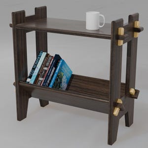 May include: A dark brown wooden shelf unit with two shelves. The shelf unit has gold accents and is holding a white mug and a stack of books.