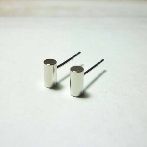 May include: A pair of silver stud earrings with cylindrical posts. The posts are smooth and have a polished finish.