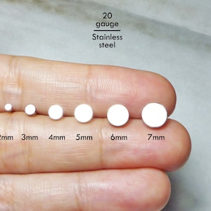 Puede incluir: Un conjunto de seis tachuelas circulares de acero inoxidable de calibre 20, ordenadas por tamaño de 2 mm a 7 mm. Cada tachuela de tono plateado presenta una cara plana y redonda, etiquetada con su medida de diámetro en milímetros debajo.