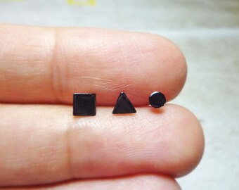May include: Three black stud earrings in the shapes of a square, triangle, and circle.