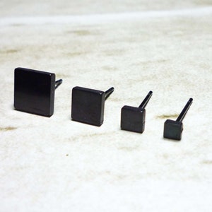 May include: Four black square stud earrings of different sizes. The earrings are made of metal and have a simple, minimalist design.