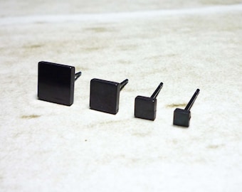 May include: Four black square stud earrings of different sizes. The earrings are made of metal and have a simple, minimalist design.