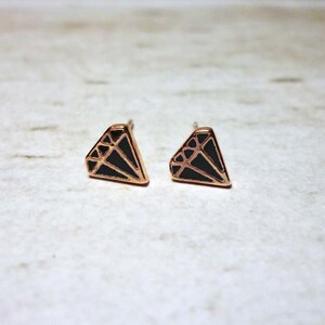 Puede incluir: Un par de pendientes de tono dorado con un diseño en forma de diamante negro.