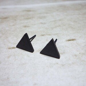 Puede incluir: Un par de pendientes de tri&aacute;ngulo negro. Los pendientes son de metal y tienen un dise&ntilde;o simple y geom&eacute;trico.