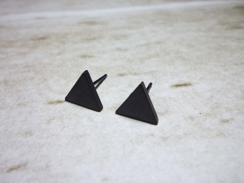 Puede incluir: Un par de pendientes de tri&aacute;ngulo negro. Los pendientes son de metal y tienen un dise&ntilde;o simple y geom&eacute;trico.