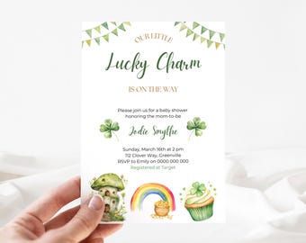 May include: A baby shower invitation with a green shamrock and rainbow design. The text reads "Our Little Lucky Charm is on the Way".