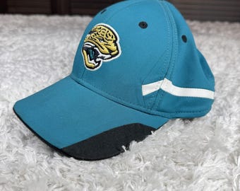 May include: Teal baseball cap featuring a team logo of a jaguar's head in yellow and black. The cap has a curved brim with a black underside, white stripes on the side, and black accents. The cap is made of a durable fabric.
