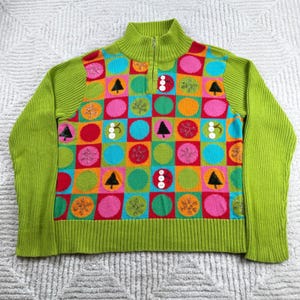 May include: A lime green quarter-zip jumper featuring a vibrant checkerboard pattern of squares and circles in shades of pink, orange, blue, and green. The design includes embroidered snowflake and pine tree motifs, with white buttons as accents.