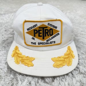 May include: White baseball cap with a yellow and black Petro logo patch. The patch reads "Recovery, Systems, Oil, Reclamation, The Specialists." The cap also features two yellow embroidered leaf designs on the brim.