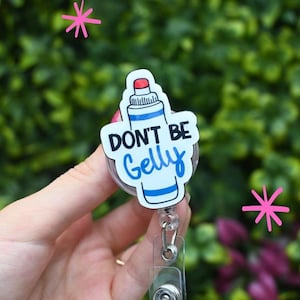 Könnte beinhalten: Ein weißes und blaues Ausweis-Rollband mit den Worten "DON'T BE Gelly" in schwarzer und blauer Schrift. Das Ausweis-Rollband hat die Form einer Geltube. Das Rollband hat einen transparenten Kunststoffclip und ein einziehbares Kabel.