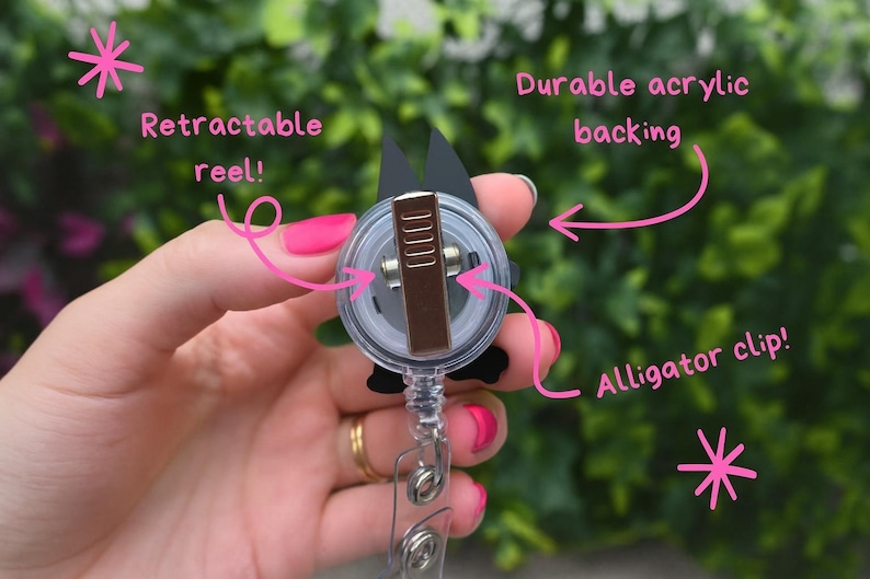 May include: A black and white badge reel with a retractable reel and alligator clip. The reel has a durable acrylic backing. The text on the image says "Retractable reel!" and "Durable acrylic backing" and "Alligator clip!"