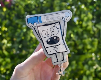 May include: A silver glitter badge holder with a cartoon character holding a blue and white pregnancy test. The character has a black outline and is drawn in a simple style. The text on the pregnancy test reads "PAY ME MY MONEY".