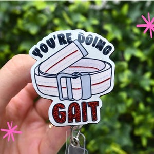May include: A white and gray badge reel with the words "YOU'RE DOING GAIT" in black and red. The badge features an illustration of a gait belt with red glitter accents. The reel has a clear plastic attachment.