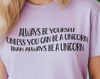 May include: A lavender t-shirt with the text "Always be yourself unless you can be a unicorn then always be a unicorn" printed in black.