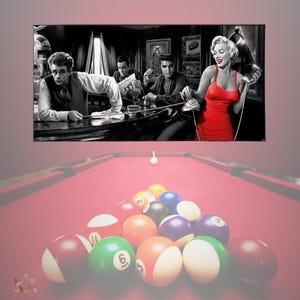 May include: A framed black and white image featuring iconic figures, including Marilyn Monroe in a red dress, above a pool table with a rack of billiard balls. The pool table has a red felt surface.