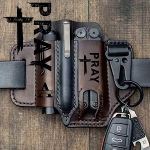 May include: A brown leather belt organizer with multiple compartments. The organizer holds a flashlight, pen, and multi-tool. The word "PRAY" and a cross are printed on the leather. A key ring with keys and a knife is attached.