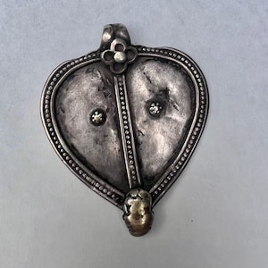 May include: A silver heart-shaped pendant with a gold accent. The pendant features a floral design at the top and two raised circles in the centre.