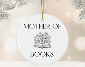 Puede incluir: Adorno navideño de cerámica blanca con texto negro que dice "Madre de libros" y una ilustración en blanco y negro de un libro con flores en la parte superior.
