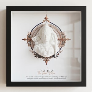 May include: A framed artwork featuring a white bust of Rama, the seventh avatar of Vishnu, set against an ornate, circular backdrop. The artwork is framed in a black square frame. Text at the bottom reads "RAMA The Ideal Man".